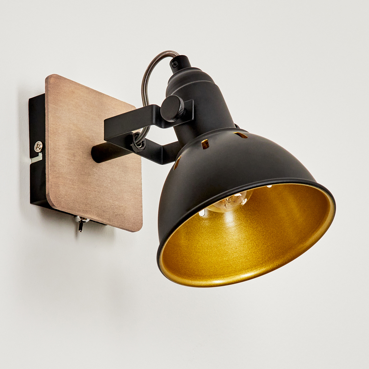 Eine schwarze Wandleuchte mit Holzsockel, goldener Innenseite und verstellbarem Arm.