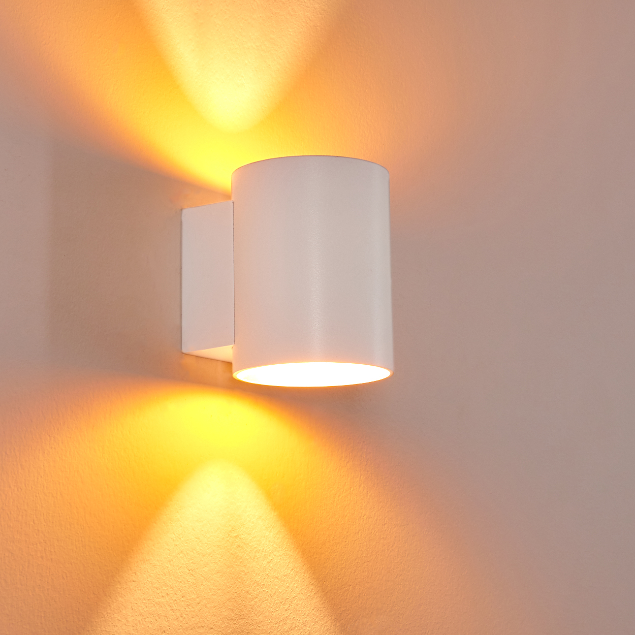 Eine weiße Wandleuchte wirft warmes Licht nach oben und unten an eine Wand.