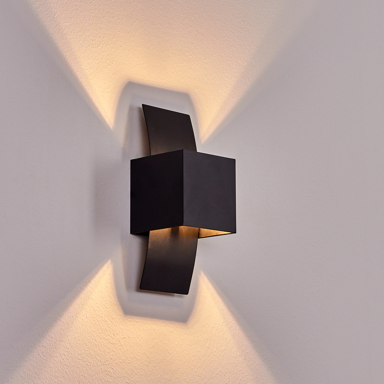 Ein schwarzer Kubus-Wandleuchter wirft nach oben und unten Licht auf eine getäfelte Wand.