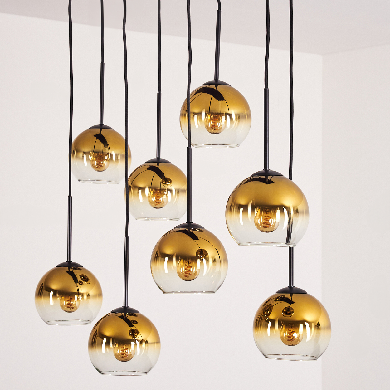 Mehrere goldene Glaskugelleuchten hängen von schwarzen Kabeln.