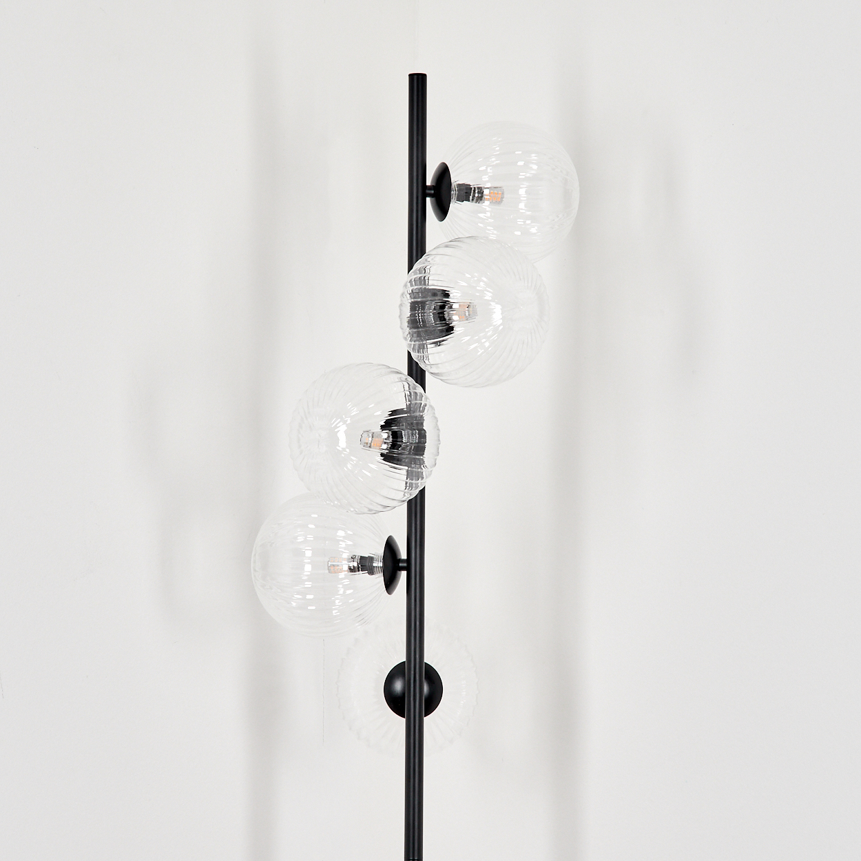 Eine vertikale schwarze Lampe mit fünf klaren, gerippten Glaskugeln und sichtbaren Glühbirnen.