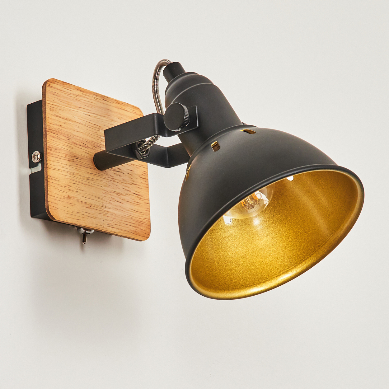 Schwarzer Wandspot mit Holzsockel und goldenem Reflektor.