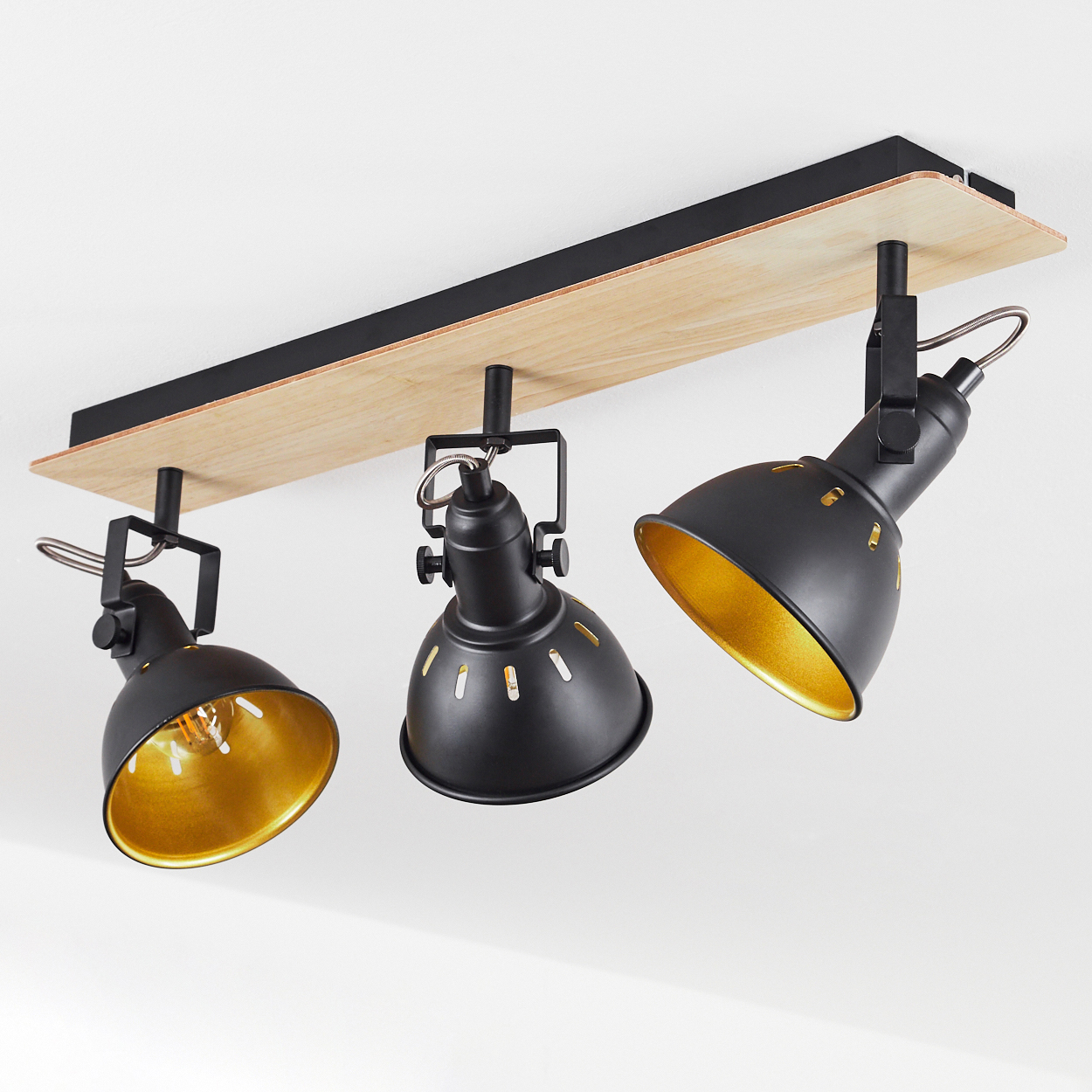 Eine schwarze Deckenleuchte mit drei verstellbaren Strahlern mit goldenem Inneren auf Holzsockel.
