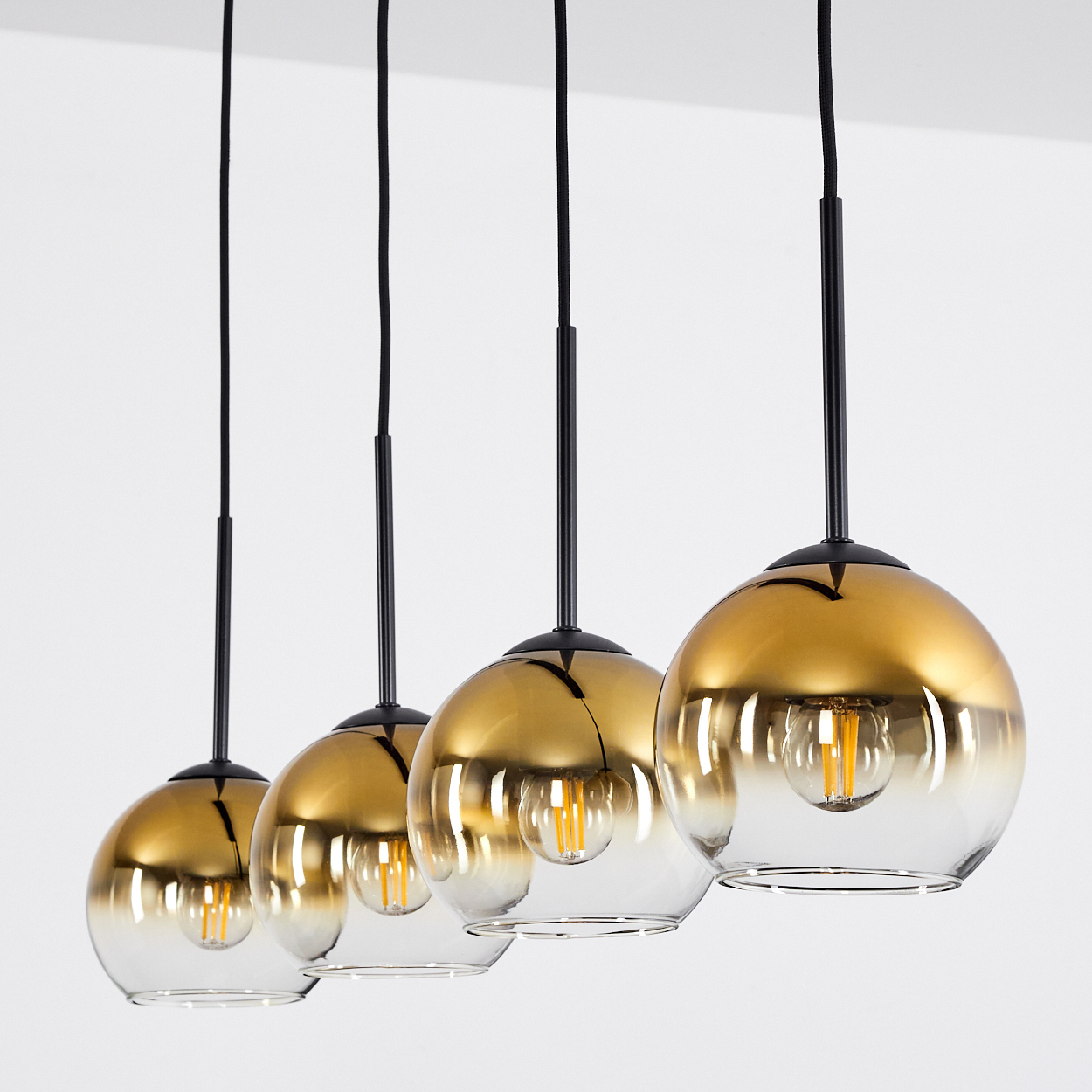 Vier goldene und durchsichtige Pendelleuchten mit sichtbaren Glühbirnen vor weißem Hintergrund.