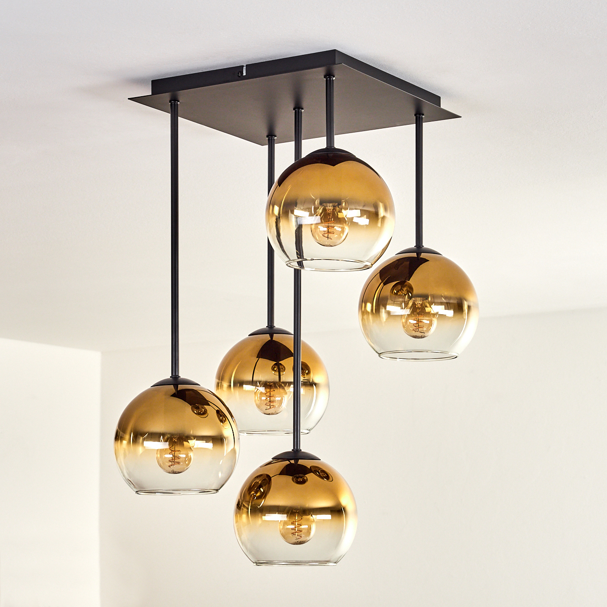 Eine Deckenleuchte mit fünf goldenen Glaskugeln und schwarzen Aufhängungen.