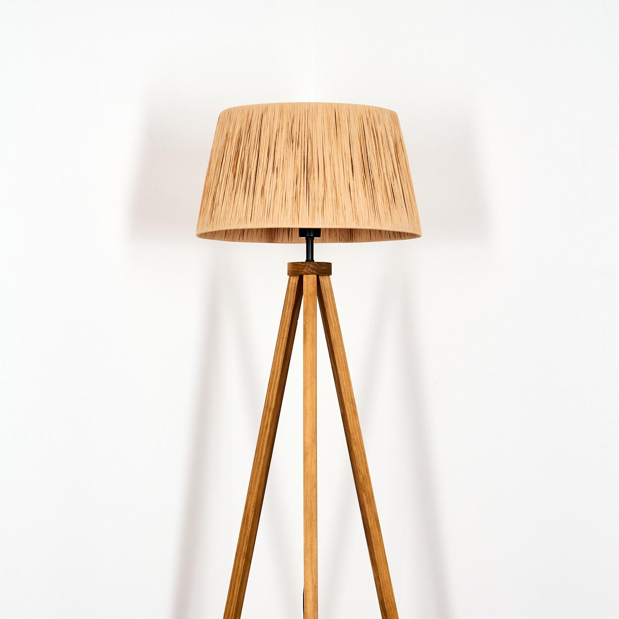 Eine hohe, moderne Stehlampe mit einem Lampenschirm aus Naturfaser und einem Holzstativ.