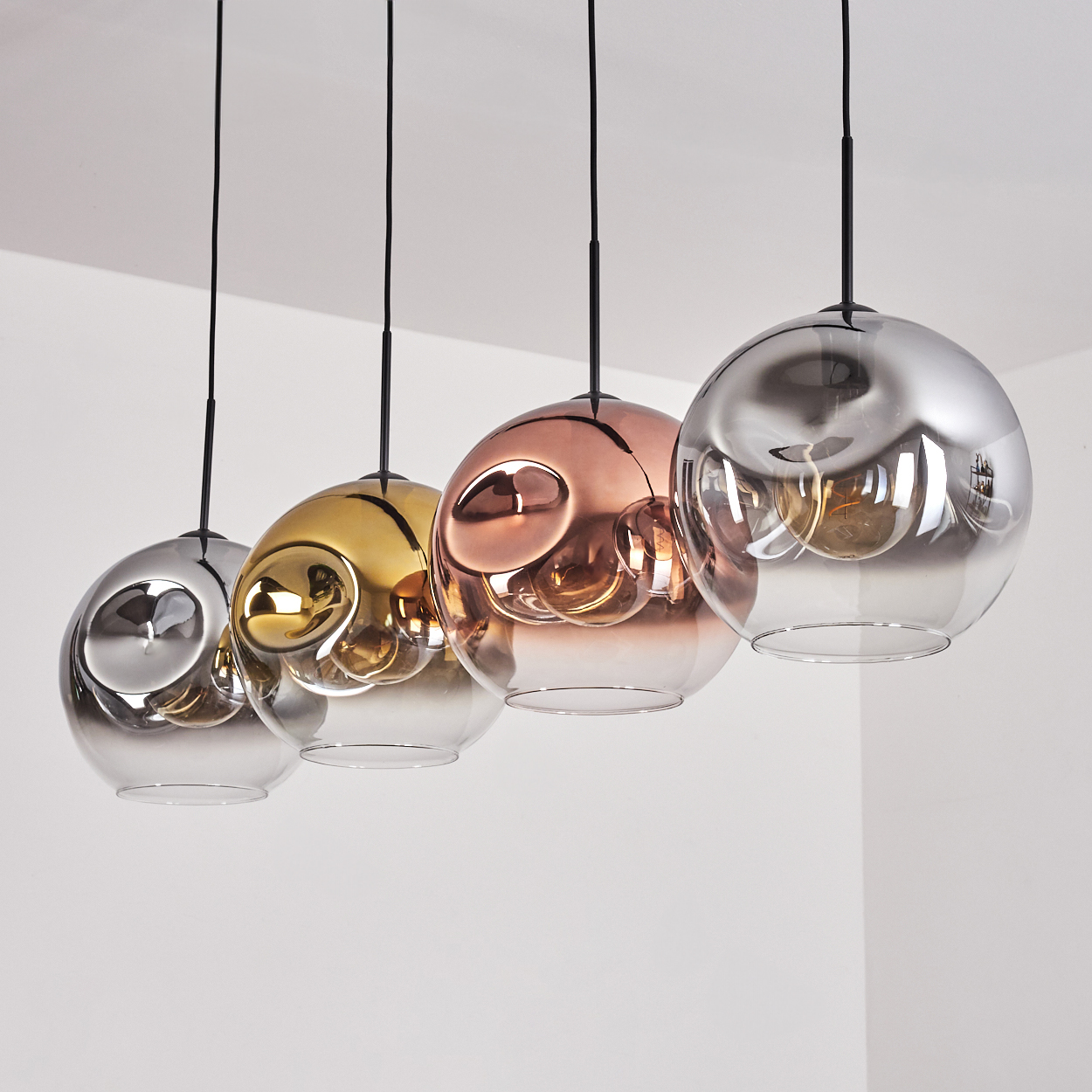 Vier Pendelleuchten mit spiegelnden, kugelförmigen Schirmen in Silber, Gold und Kupfer.