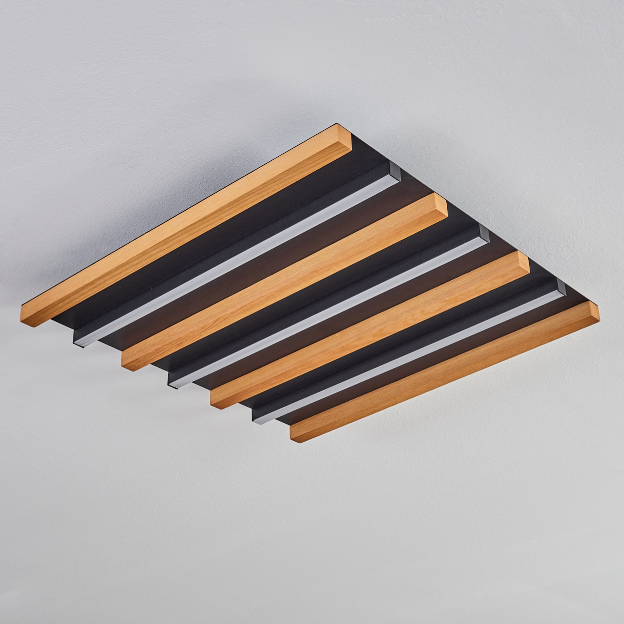 Akustikpaneel mit Holz- und schwarzen Lamellen an einer weißen Decke.