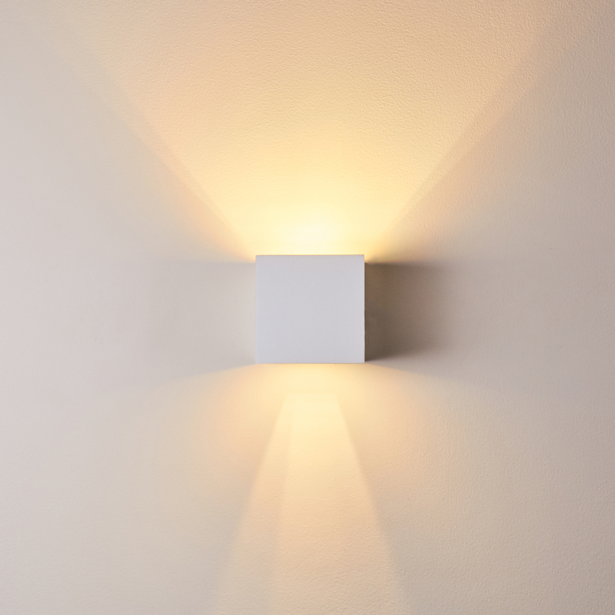 Ein weißes, würfelförmiges Wandlicht strahlt nach oben und unten Licht aus.