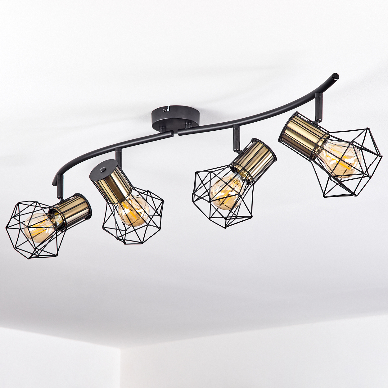 Eine schwarze gebogene Schienenleuchte mit vier verstellbaren Lampen, jede mit goldener Fassung und geometrischem Käfig.