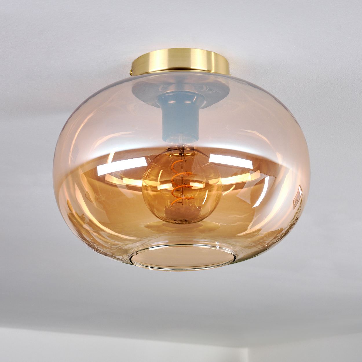 Eine bernsteinfarbene Glaskugel mit einer Edison-Glühbirne innen an der Decke montiert.