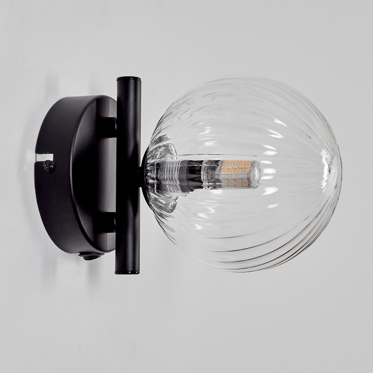 Eine schwarze Wandleuchte mit einer gerippten Glaskugel und sichtbarer LED.