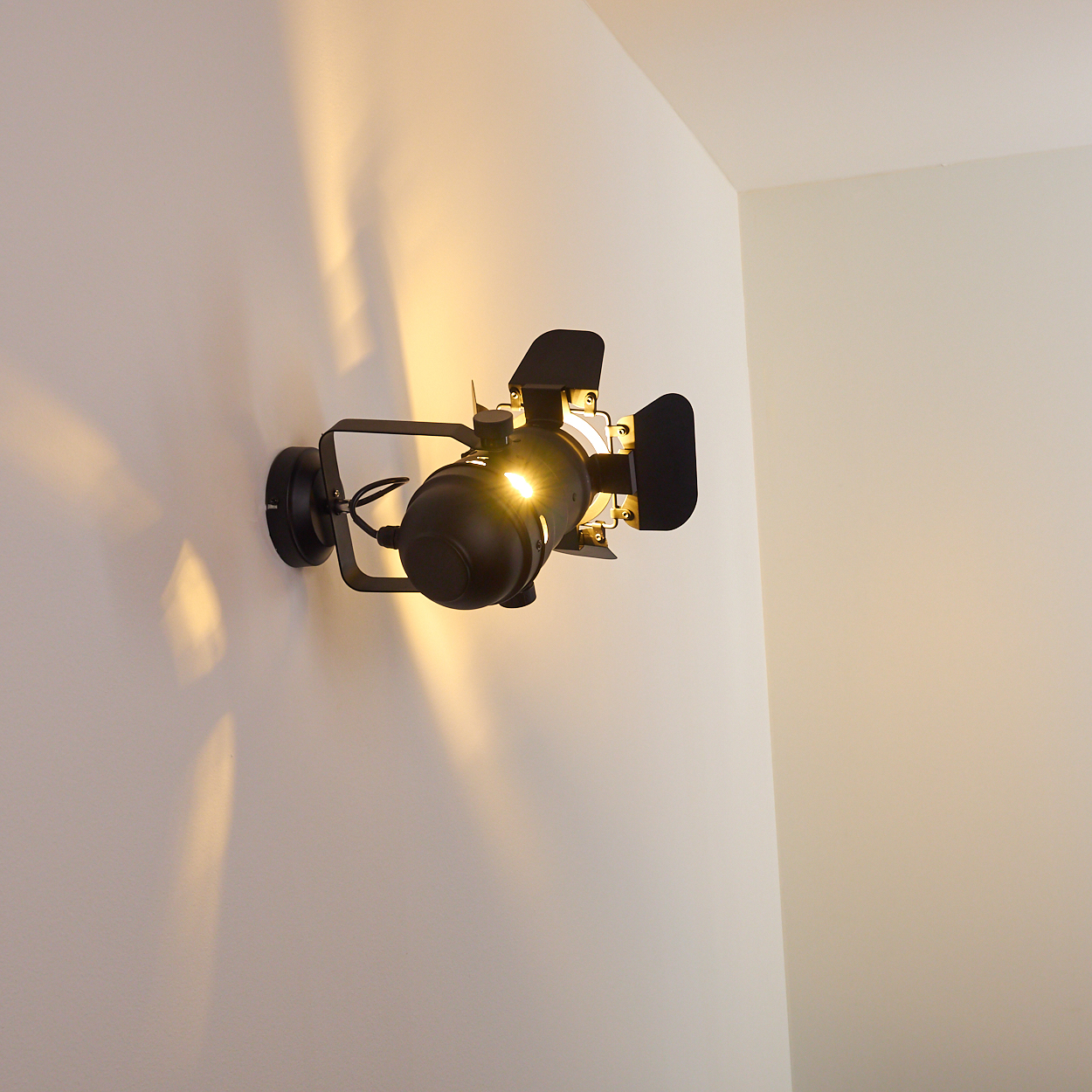 Ein schwarzer Scheinwerfer mit Klappen ist an einer weißen Wand montiert.