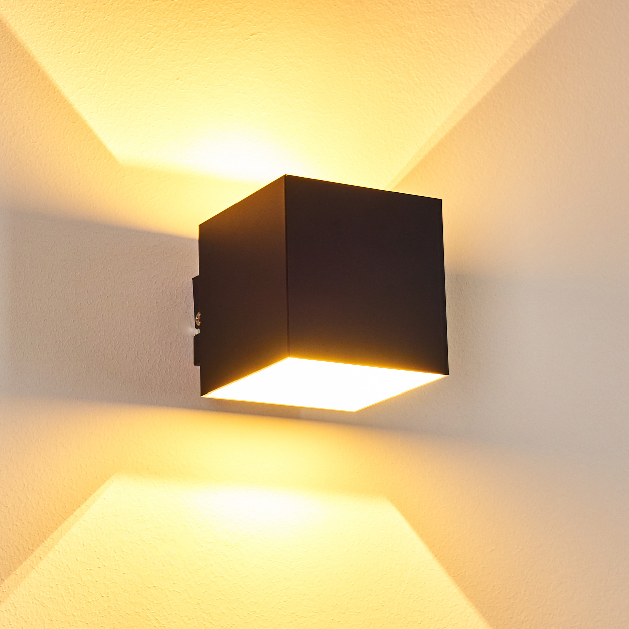 Ein schwarzer Würfel-Wandstrahler leuchtet nach oben und unten an einer weißen Wand.