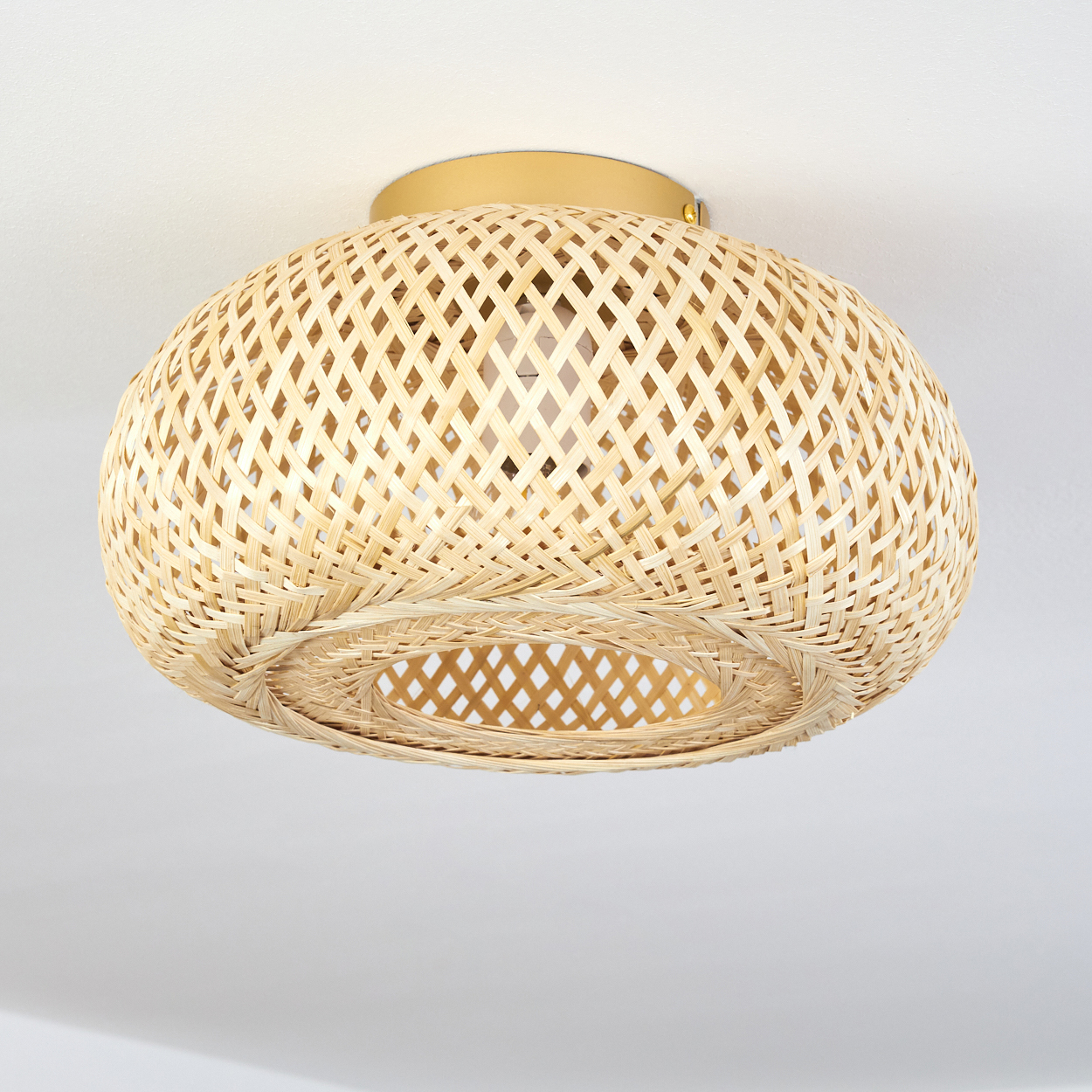 Eine runde, geflochtene Bambuslampe mit einem goldenen Baldachin an einer weißen Decke.