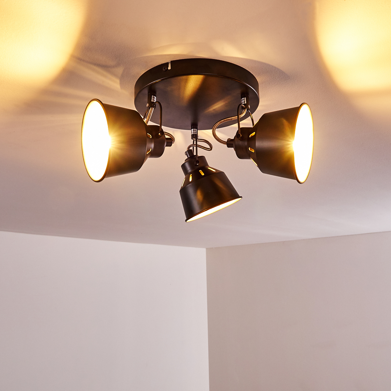 Eine schwarze Deckenleuchte mit drei verstellbaren Strahlern, die die weiße Decke beleuchten.