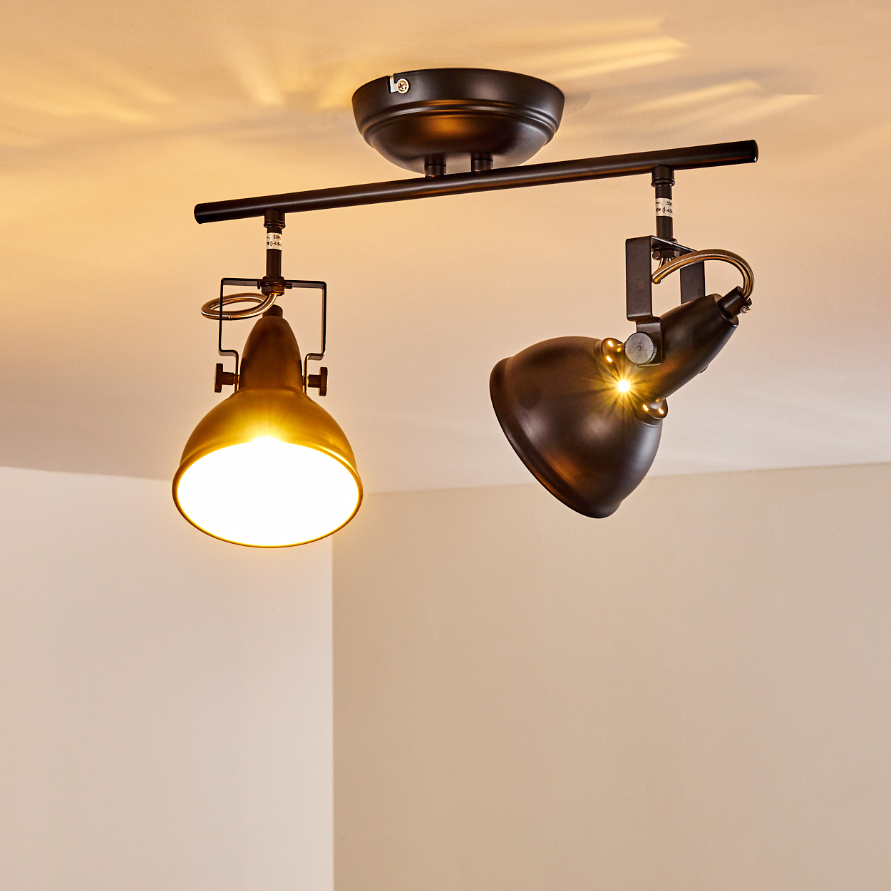 Zwei schwarze Deckenstrahler mit verstellbaren Köpfen, einer leuchtet hell.