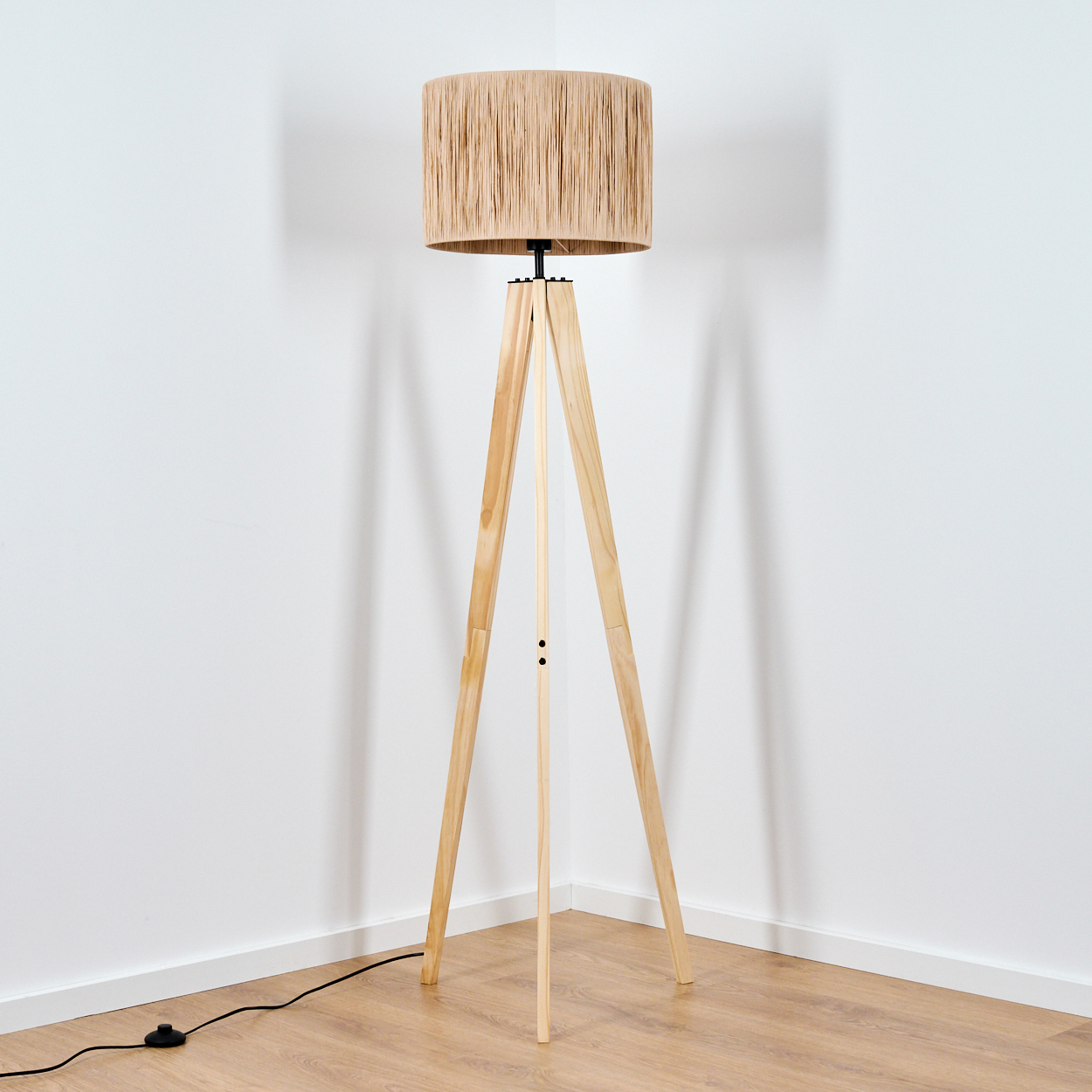Ein Stehlampe mit dreibeinigem Holzfuß und einem geflochtenen Lampenschirm.