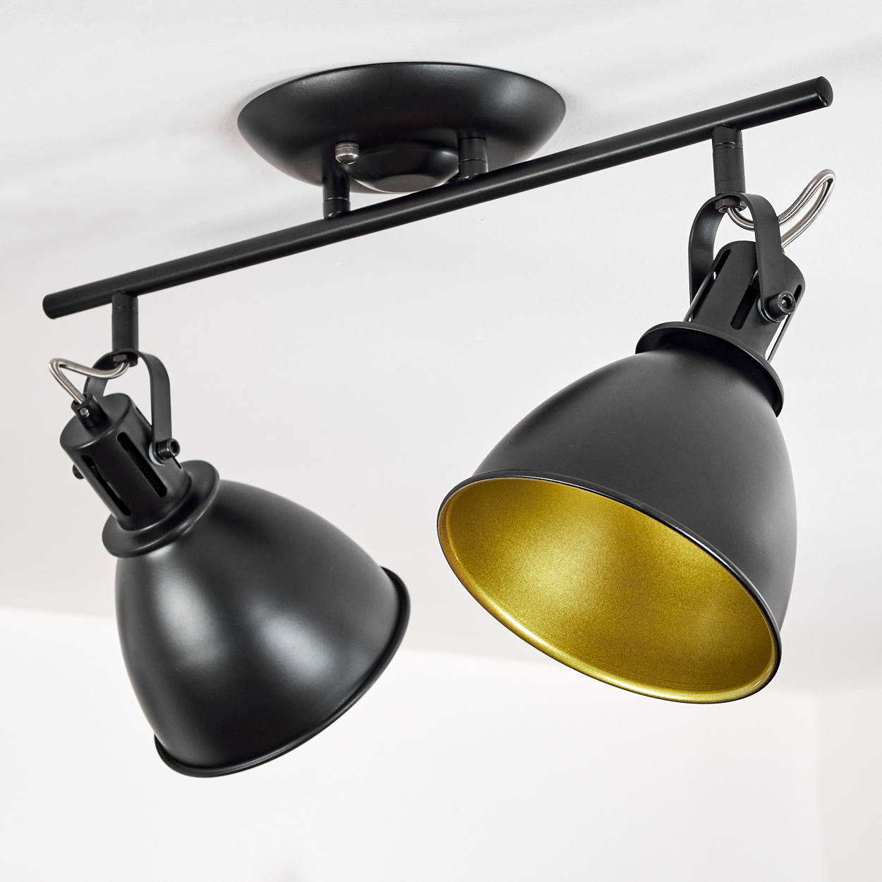 Zwei schwarze Deckenstrahler mit goldenen Innenseiten auf einer schwarzen Schiene.