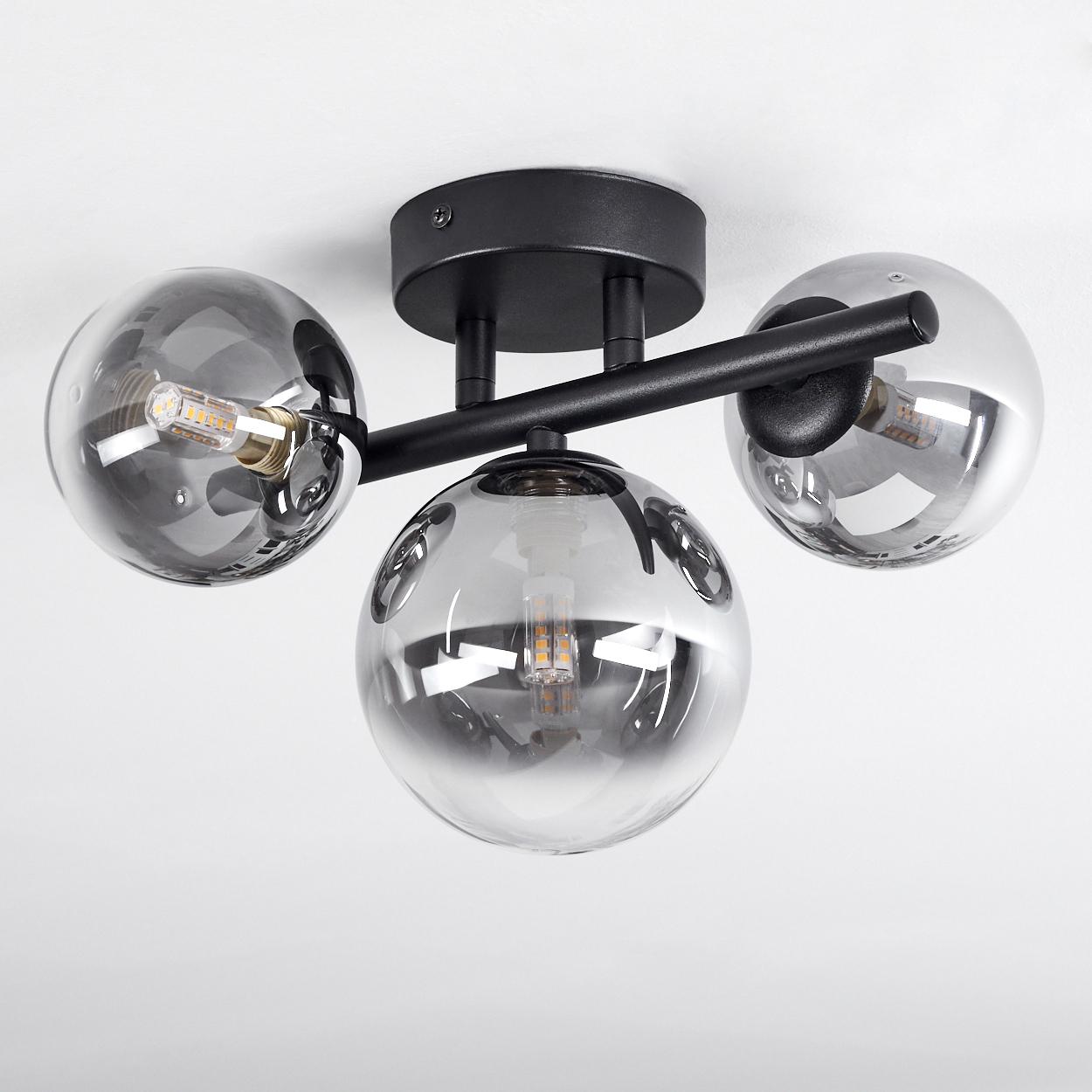 Schwarze Deckenleuchte mit drei rauchgrauen Glaskugeln und sichtbaren LED-Lampen.