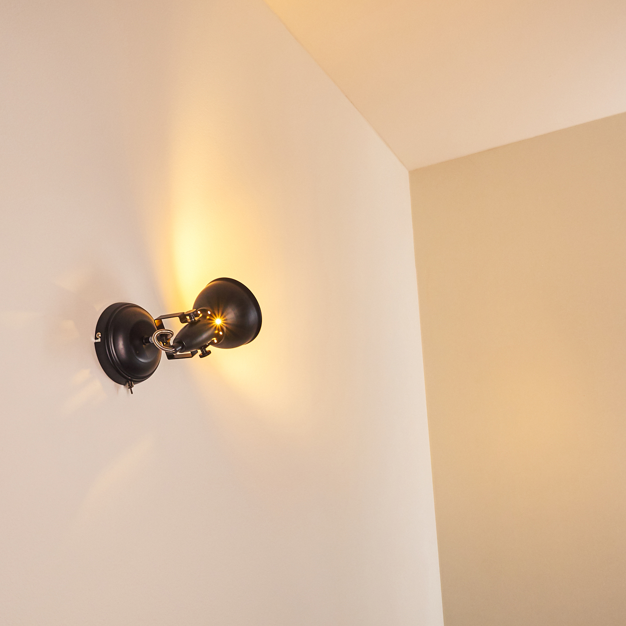 Ein schwarzer Wandspot leuchtet auf einer hellen Wand.