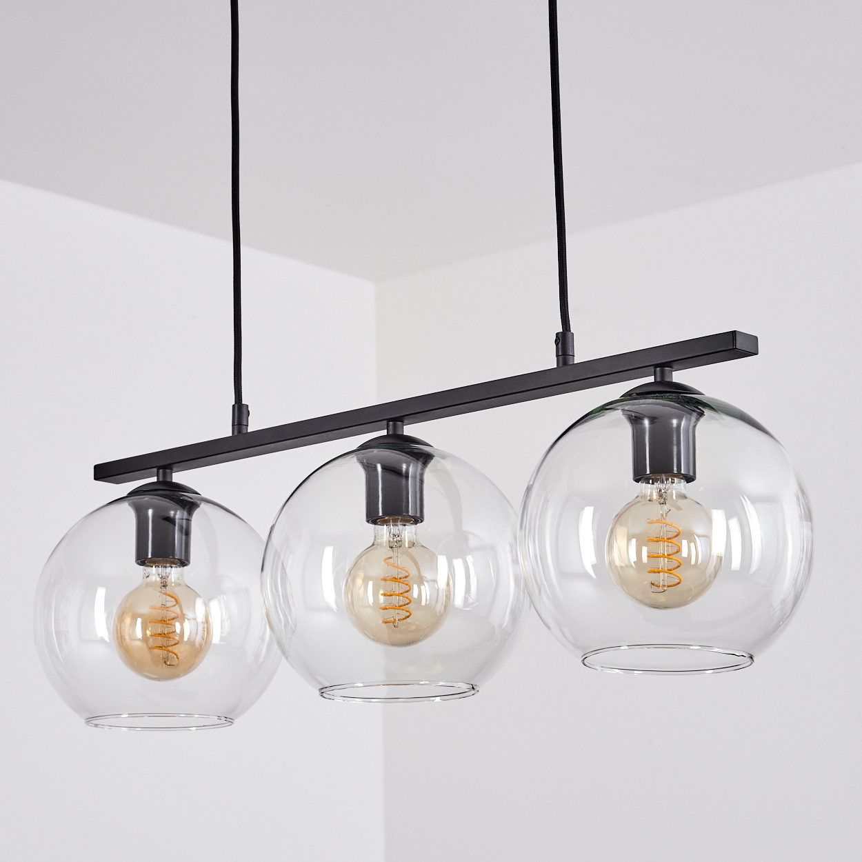 Ein moderner schwarzer Kronleuchter mit drei klaren Glaskugeln und Edison-Glühbirnen.