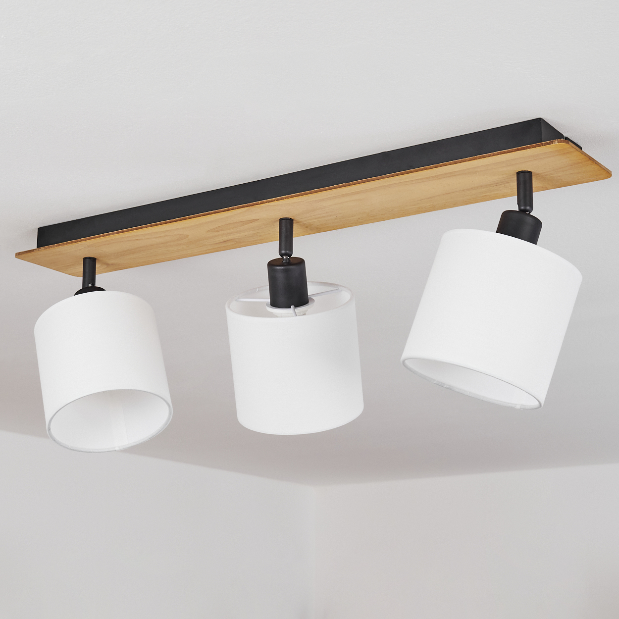Moderne Deckenleuchte mit Holzleiste, schwarzen Metallakzenten und drei weißen Zylinderschirmen.
