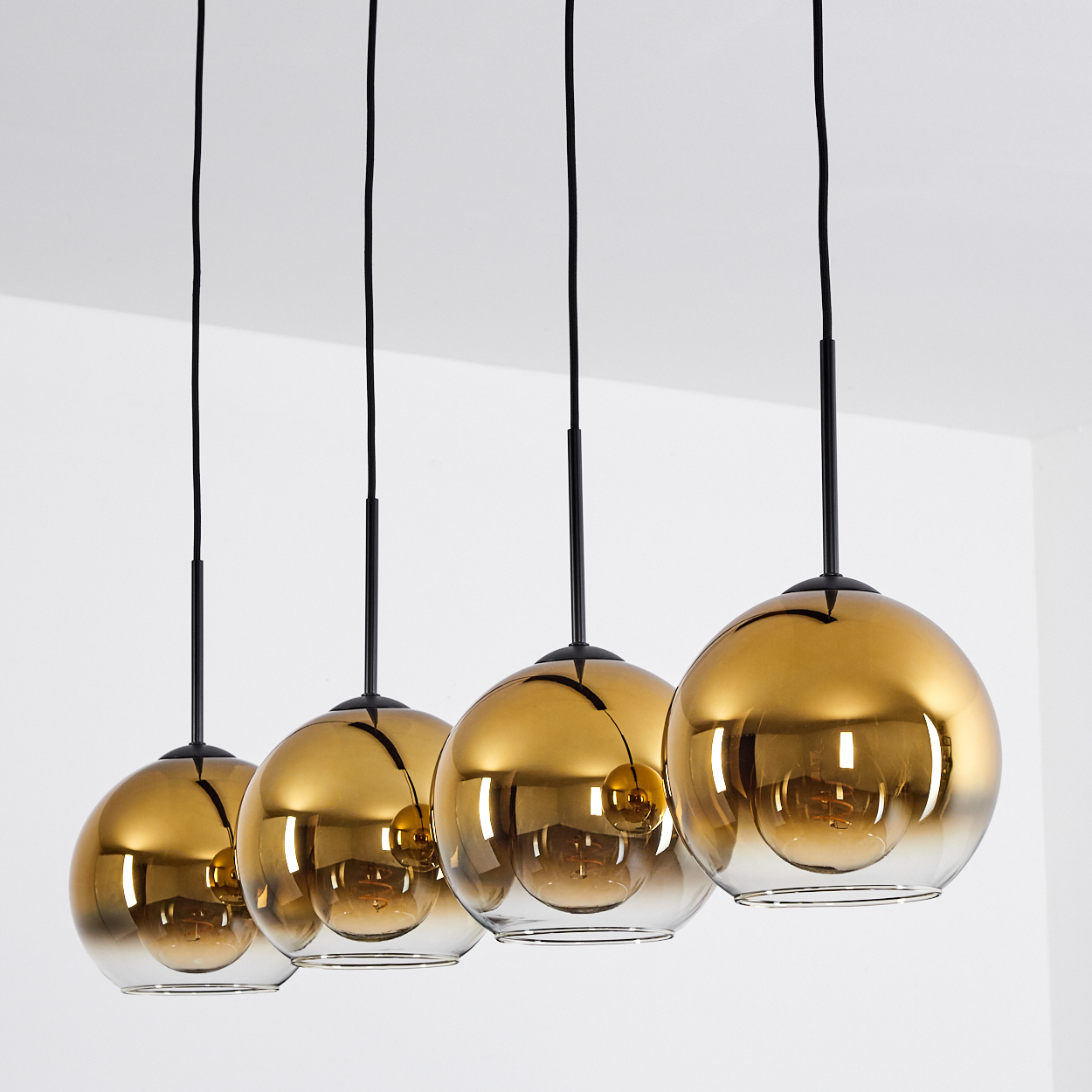Vier goldene Pendelleuchten mit Glaskugeln hängen an schwarzen Kabeln.