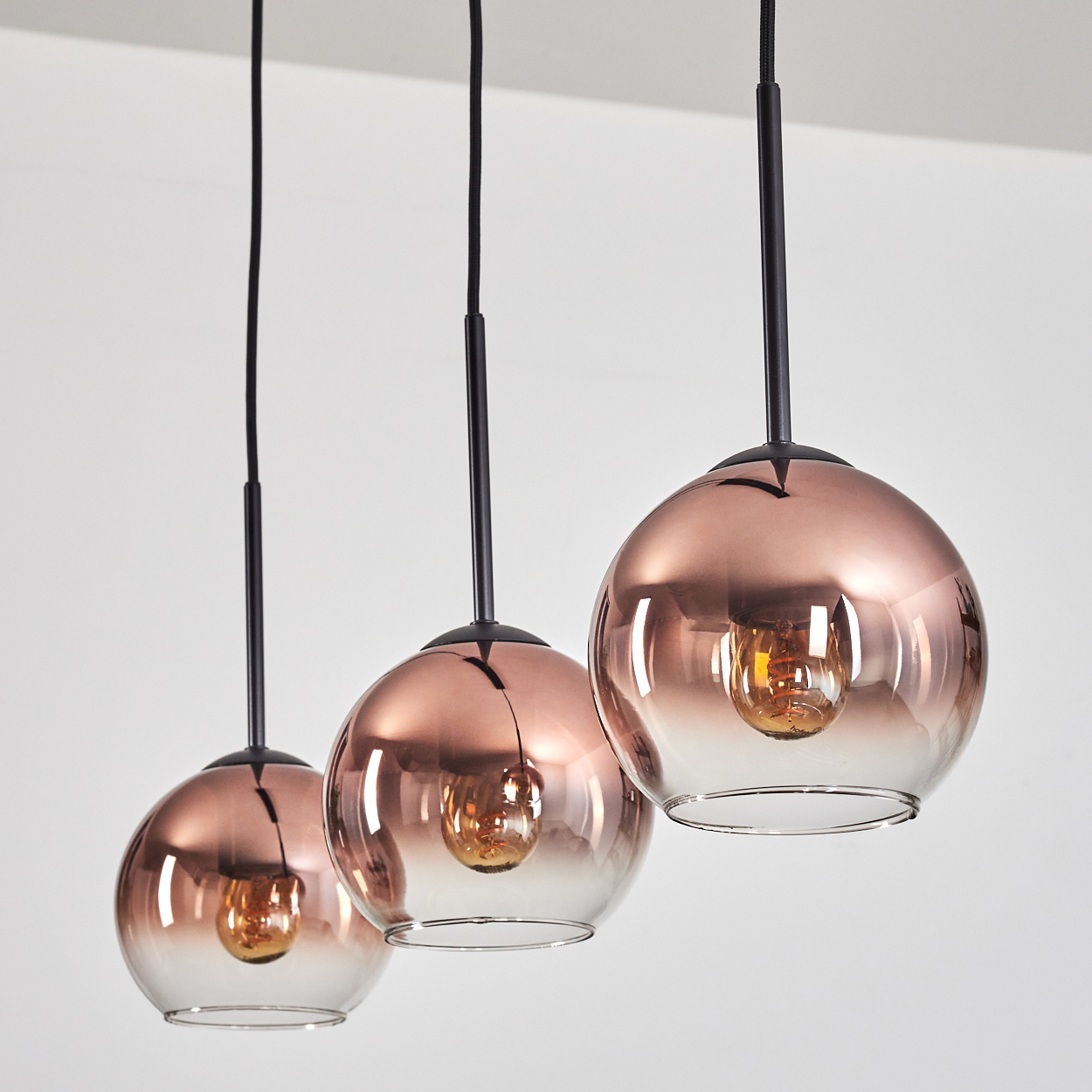 Drei kupferfarbene Pendelleuchten mit Glaslampenschirmen und sichtbaren Glühbirnen.