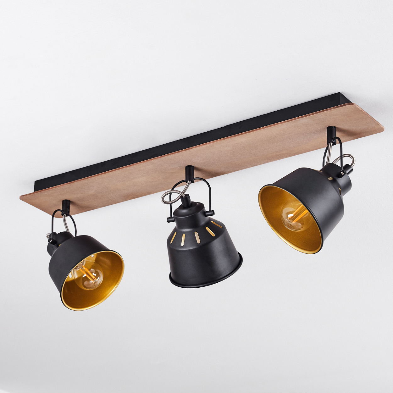 Ein schwarzer Deckenstrahler mit drei Lichtern und goldenem Innenleben auf Holzsockel.