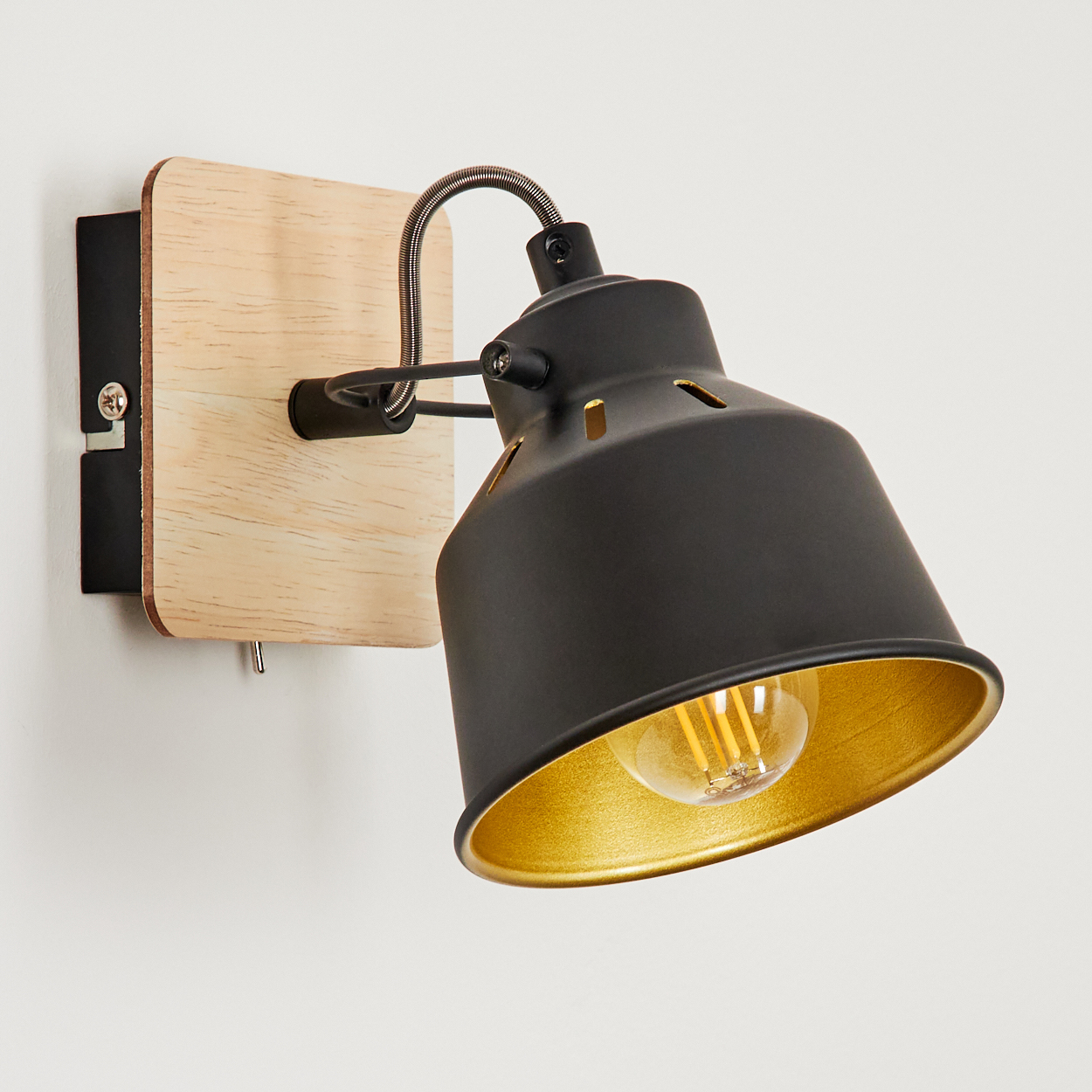 Eine schwarze Wandleuchte mit Holzsockel und goldenem Schirm.