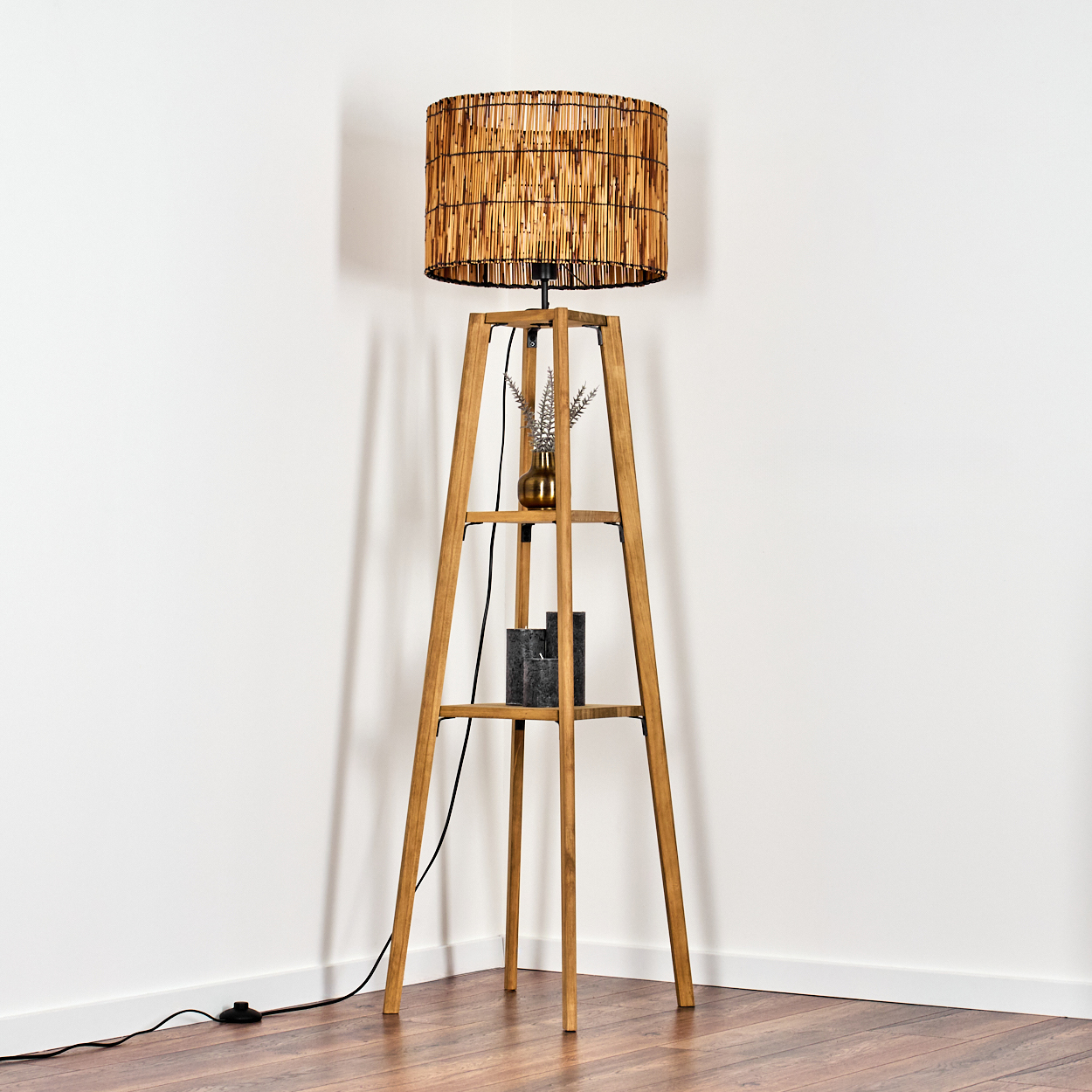 Holz-Stehlampe mit gewebtem Schirm, kleiner Vase mit Pflanzen und Kerzen auf Regalen.