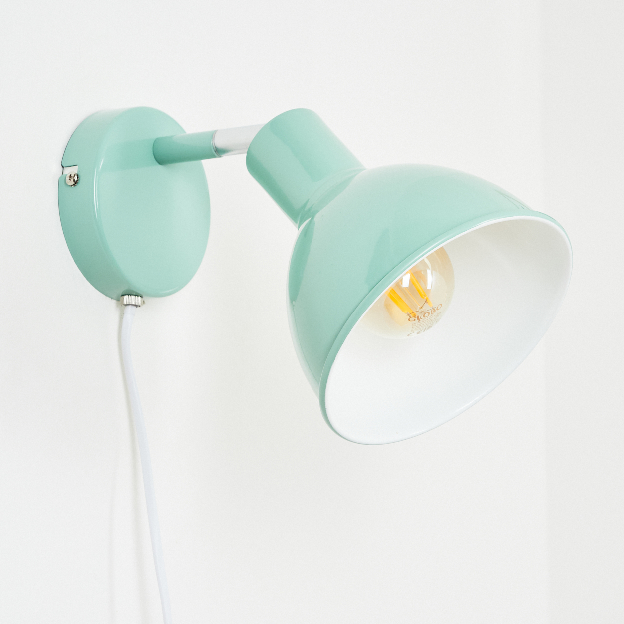 Eine mintgrüne Wandleuchte mit weißem Kabel und Glühbirne an einer weißen Wand.