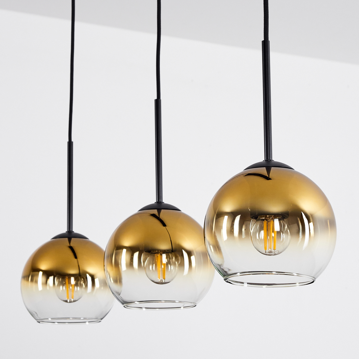 Drei moderne Pendelleuchten mit goldgetönten Glaskugeln und sichtbaren Glühbirnen.