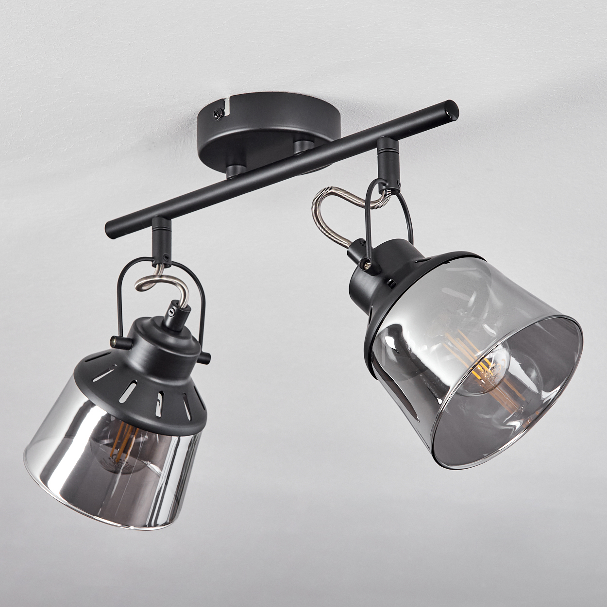 Eine schwarze Deckenleuchte mit zwei rauchglas Lampenschirmen und sichtbaren Glühbirnen.
