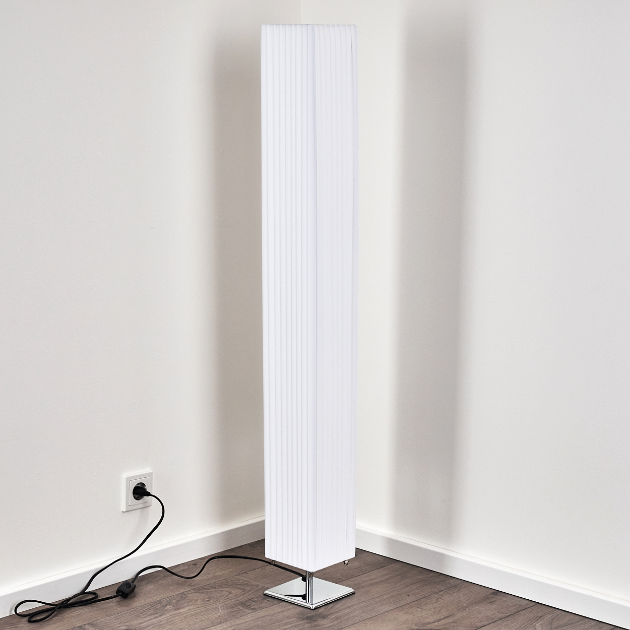 Eine weiße Stehlampe mit geripptem Schirm steht in einer Ecke auf einem Holzboden.