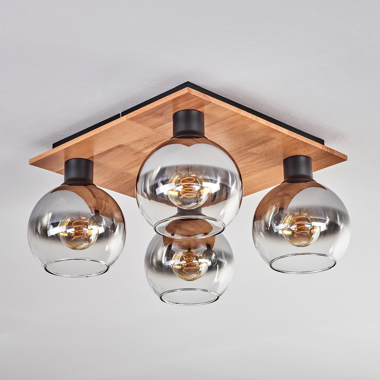 Eine moderne Deckenleuchte mit Holzsockel und vier Glaskugelschirmchen mit Edison-Glühbirnen.