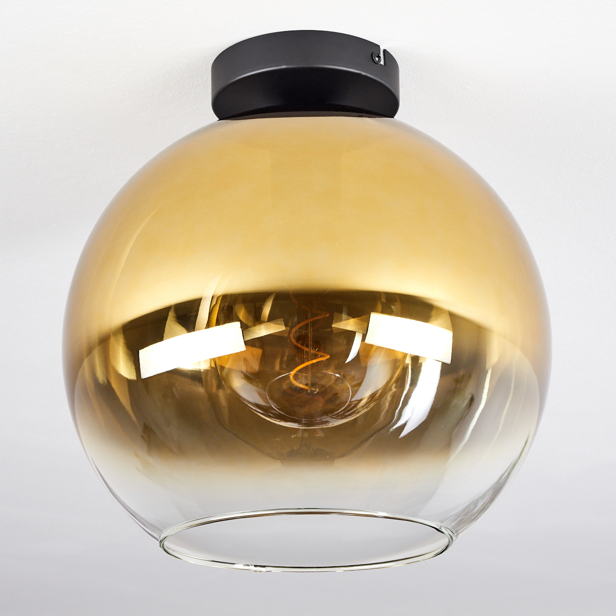 Eine goldene Glaslampe mit schwarzer Halterung und sichtbarer Glühbirne.