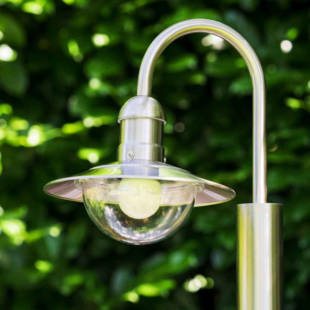Eine silberne Außenlampe mit Glasschirm ist vor unscharfem grünen Hintergrund beleuchtet.