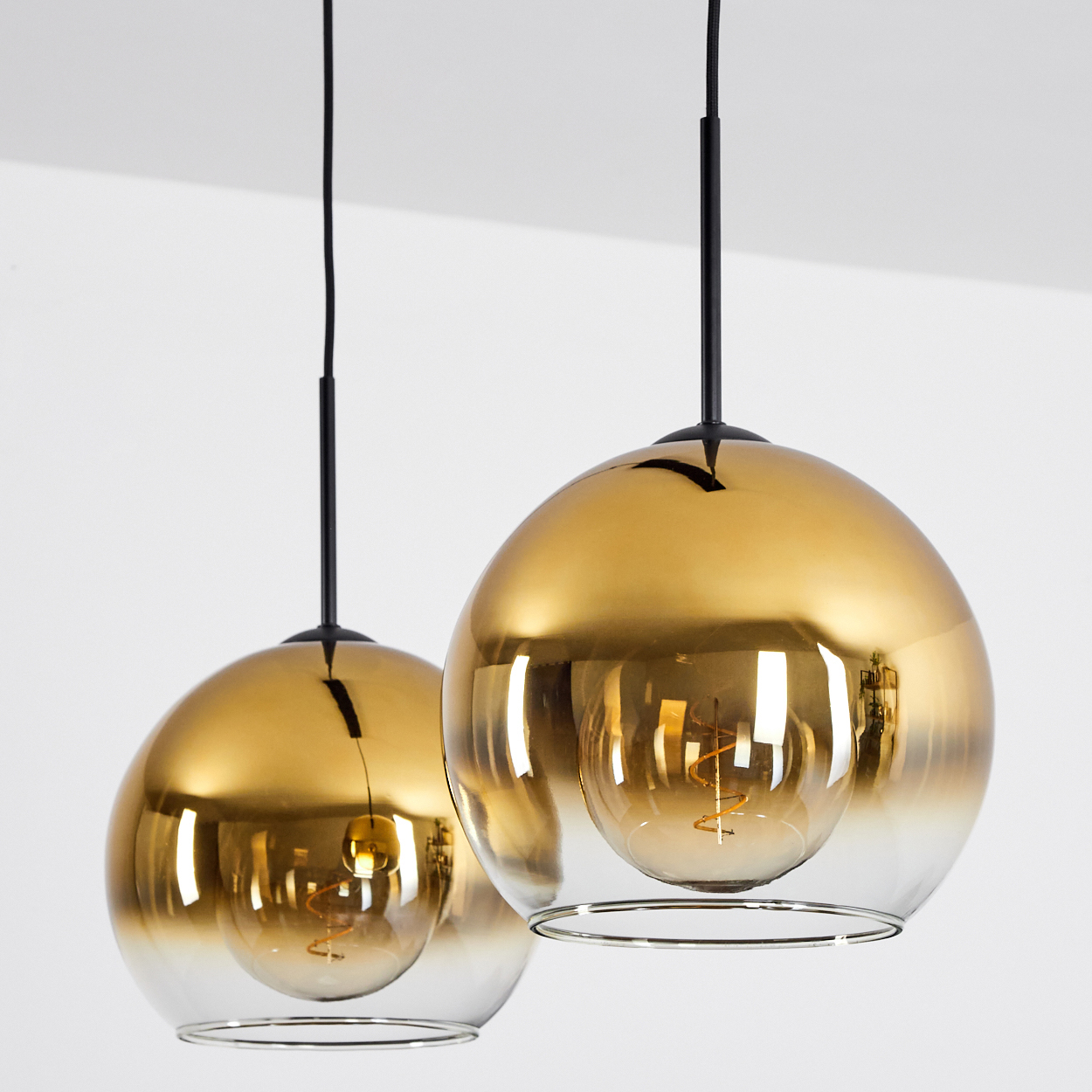 Zwei goldene Pendelleuchten mit Glühbirnen hängen von schwarzen Kabeln.