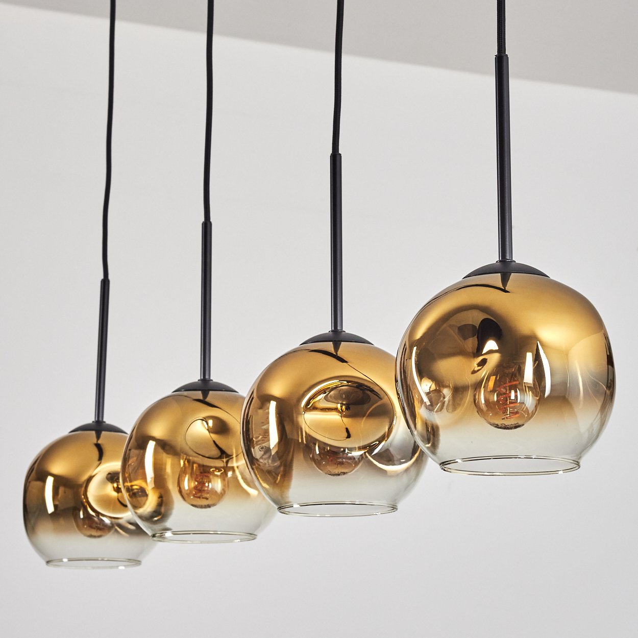 Vier goldene Hängeleuchten mit Glaskugeln und sichtbaren Glühbirnen nebeneinander.