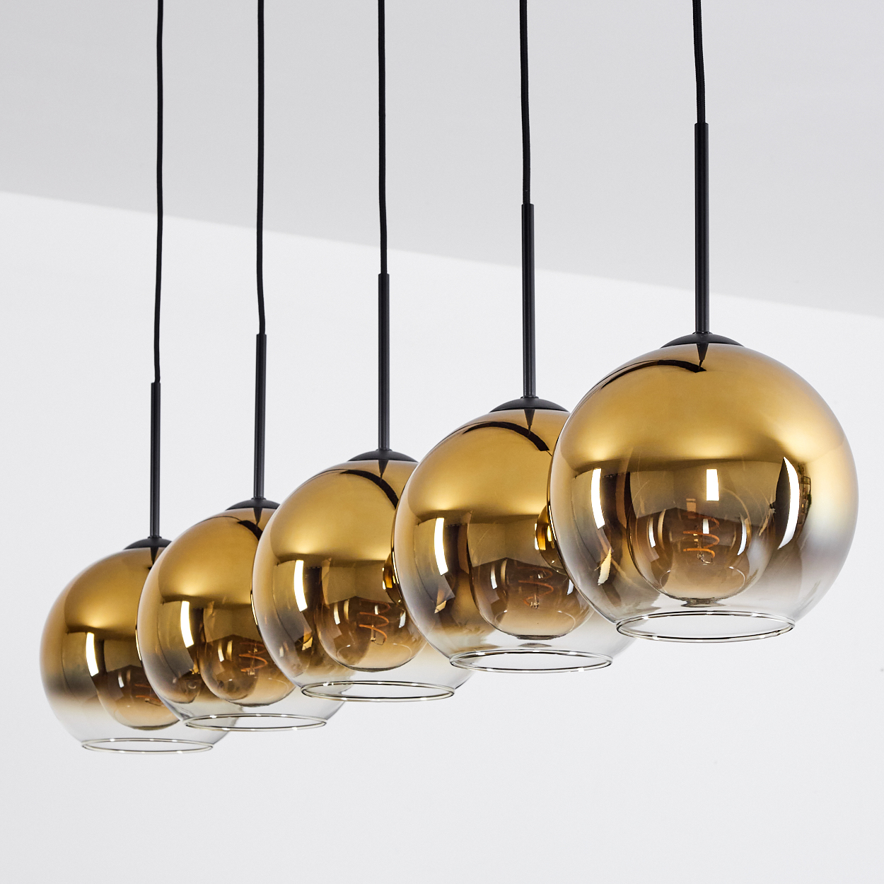 Eine Reihe von fünf goldenen Kugelleuchten mit schwarzen Kabeln vor weißem Hintergrund.