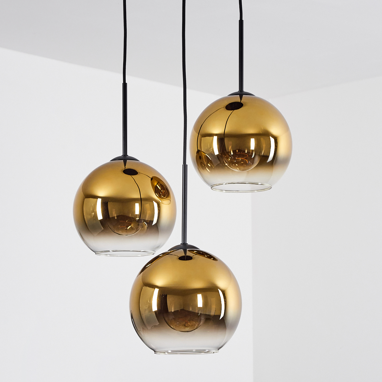 Drei goldene Hängeleuchten mit Glaskugeln, die nach unten hin transparent werden.
