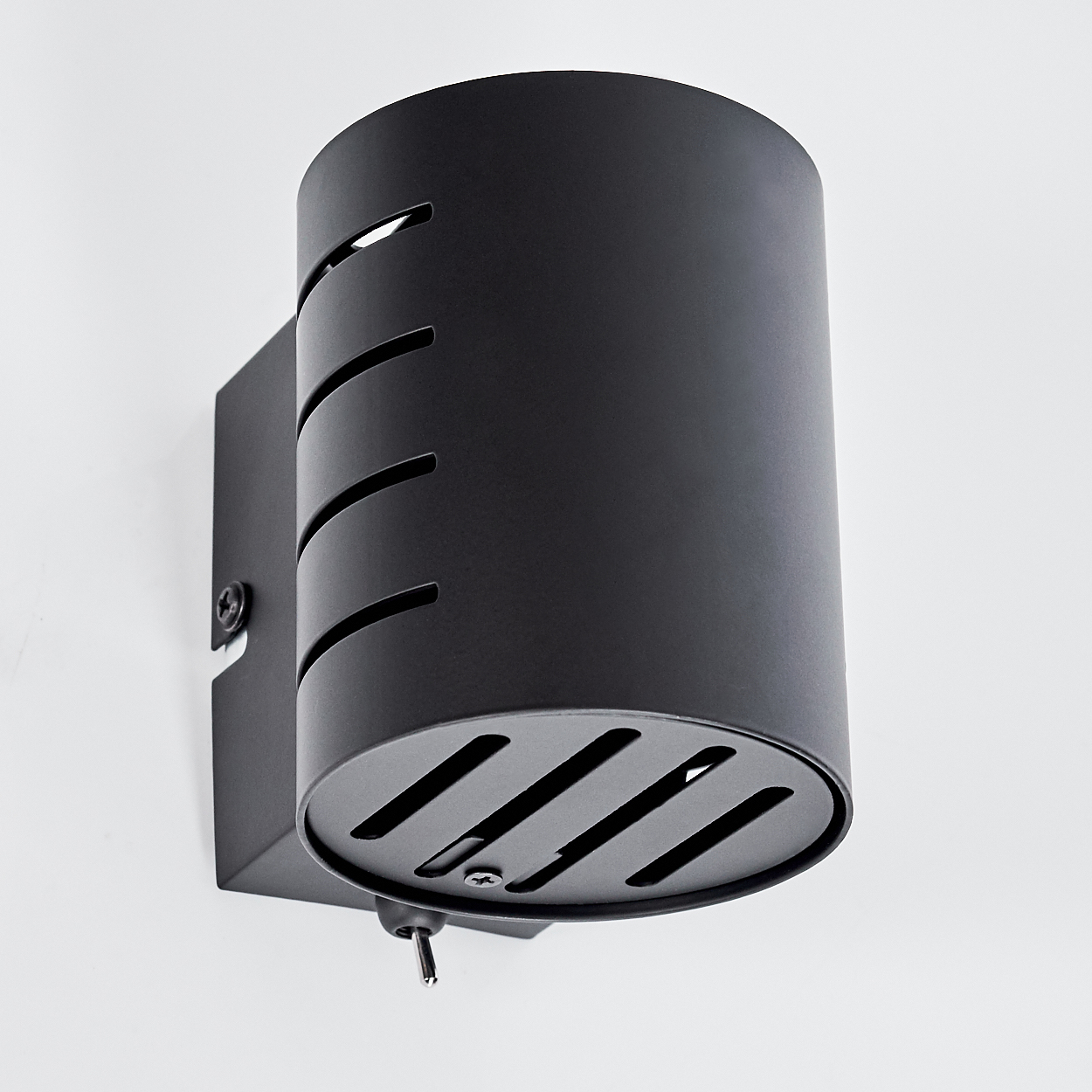 Schwarze Wandleuchte mit zylindrischem Lampenschirm und Schlitzen an der Unterseite.