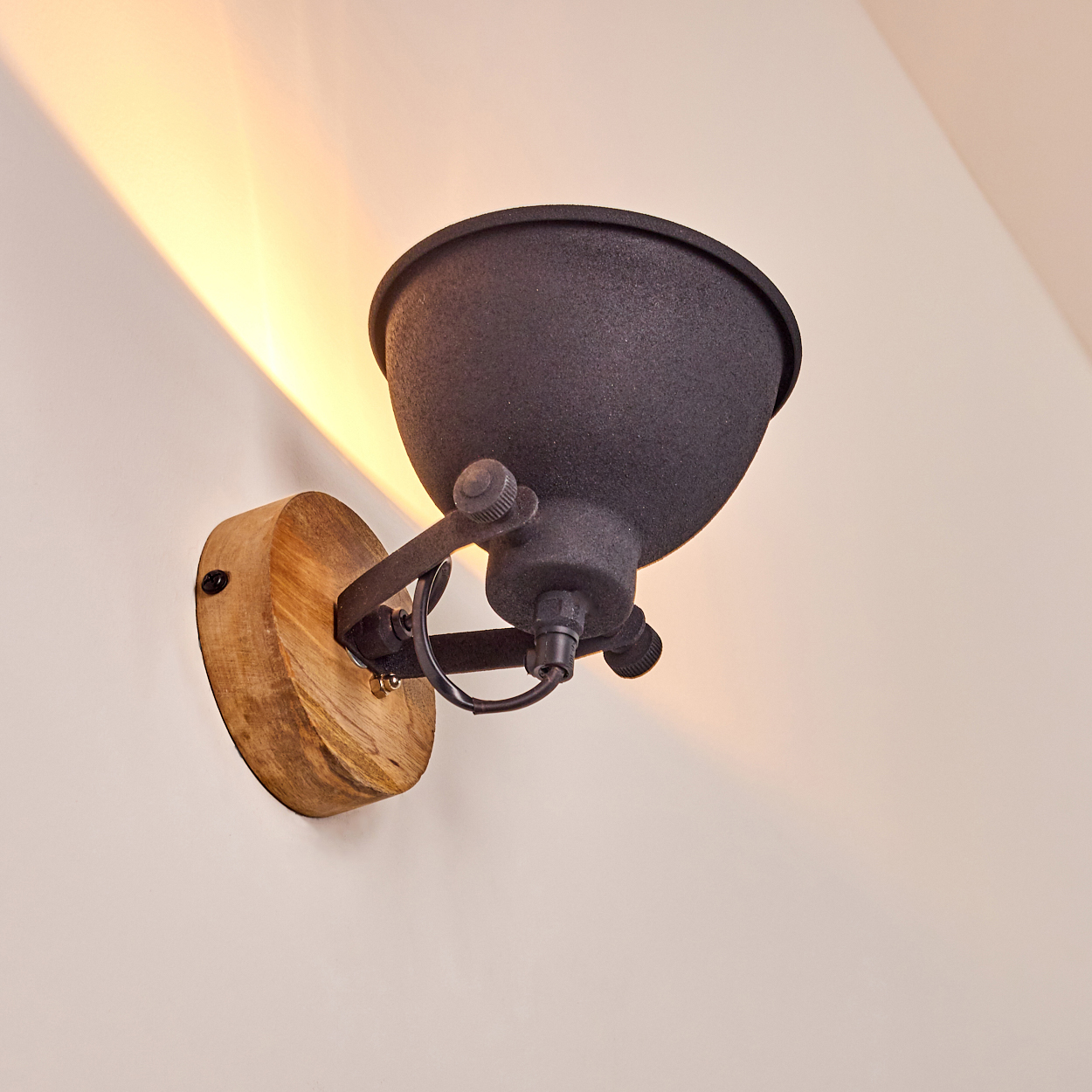 Ein schwarzer Wandlampenschirm aus Metall mit Holzsockel wirft Licht an die Wand.