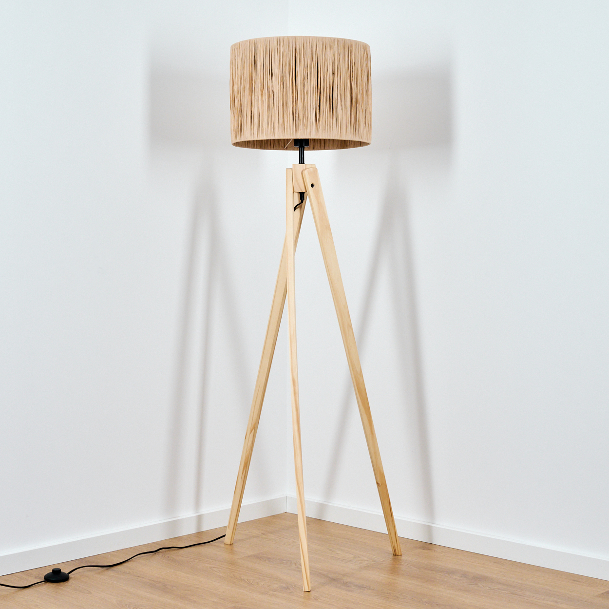 Ein Stehlampe mit einem Lampenschirm aus beige Garn und drei Holzbeinen.