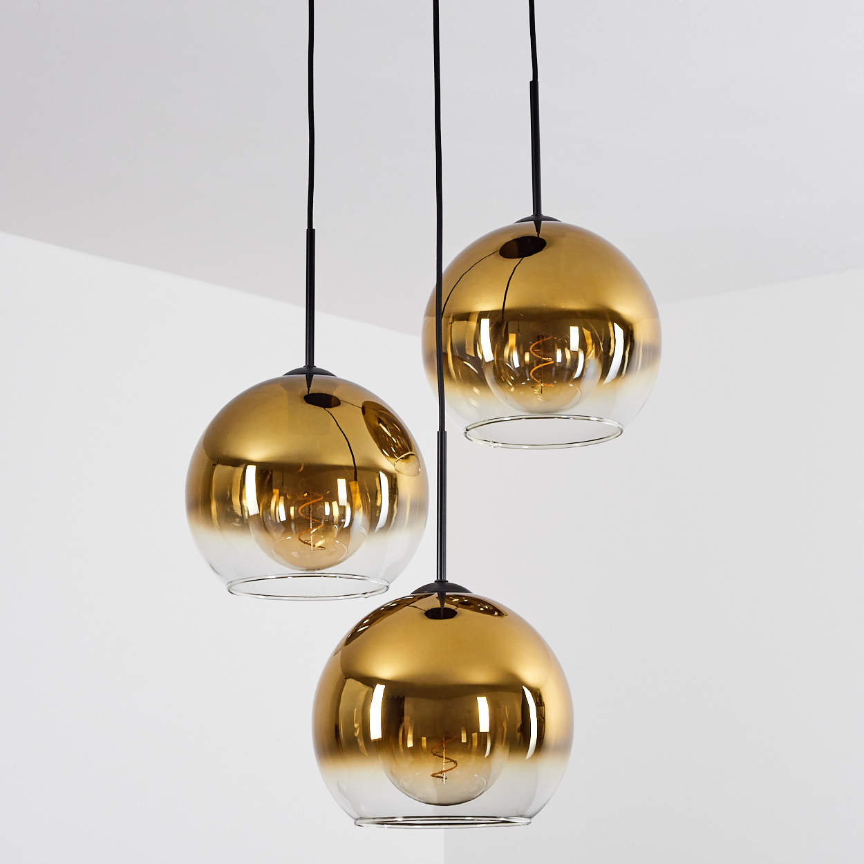 Drei goldene Pendelleuchten mit Glühbirnen hängen von schwarzen Kabeln.