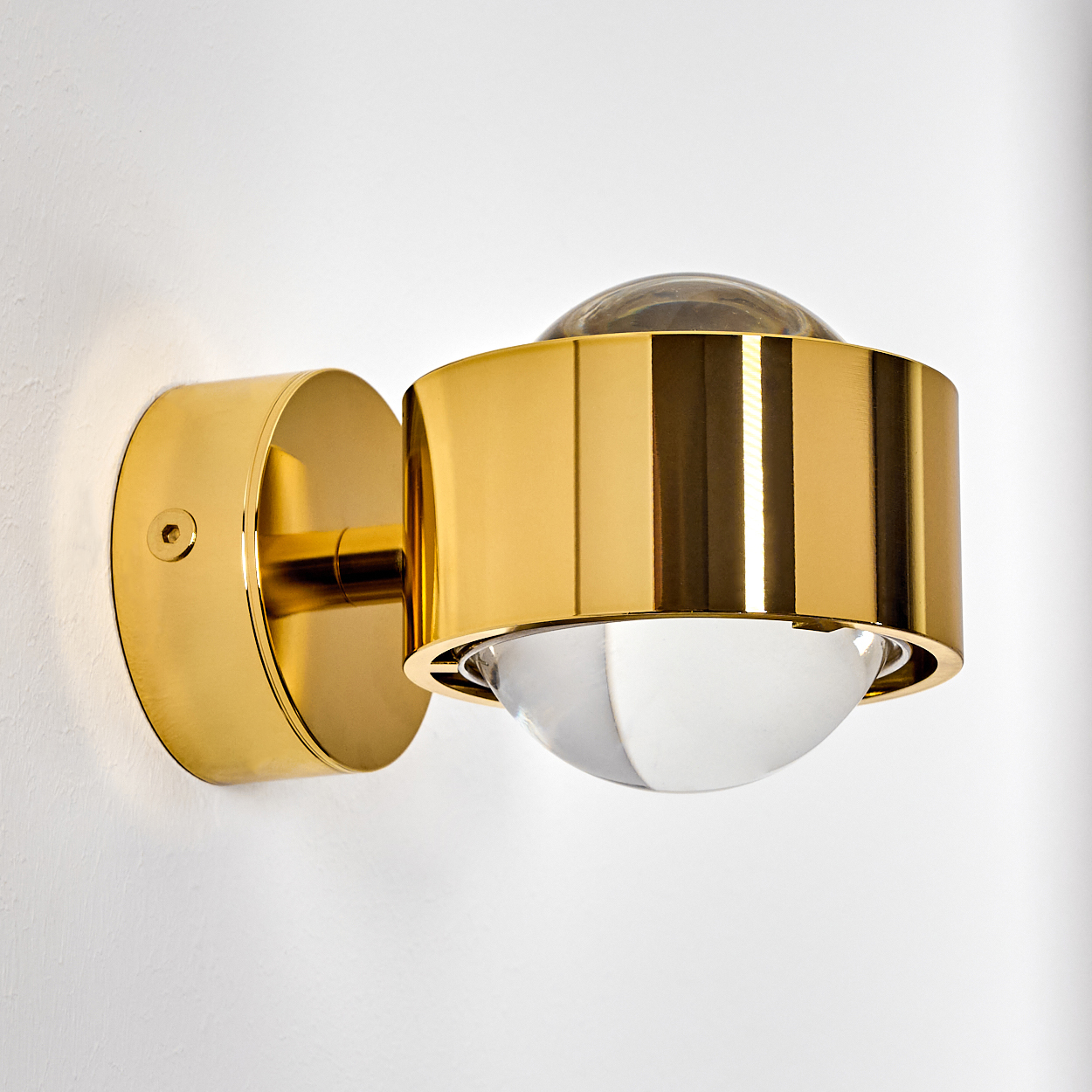 Eine goldene Wandleuchte mit klarem Glaskolben, montiert an einer weißen Wand.