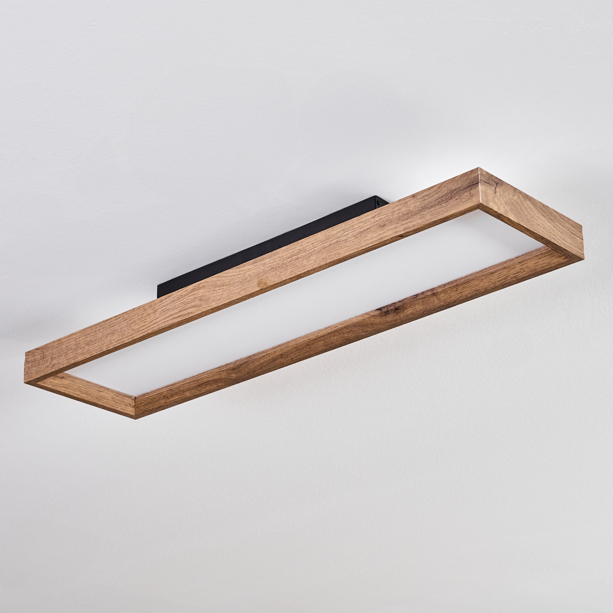 Eine rechteckige Deckenleuchte mit Holzrahmen und weißem Diffusor an einer weißen Decke.