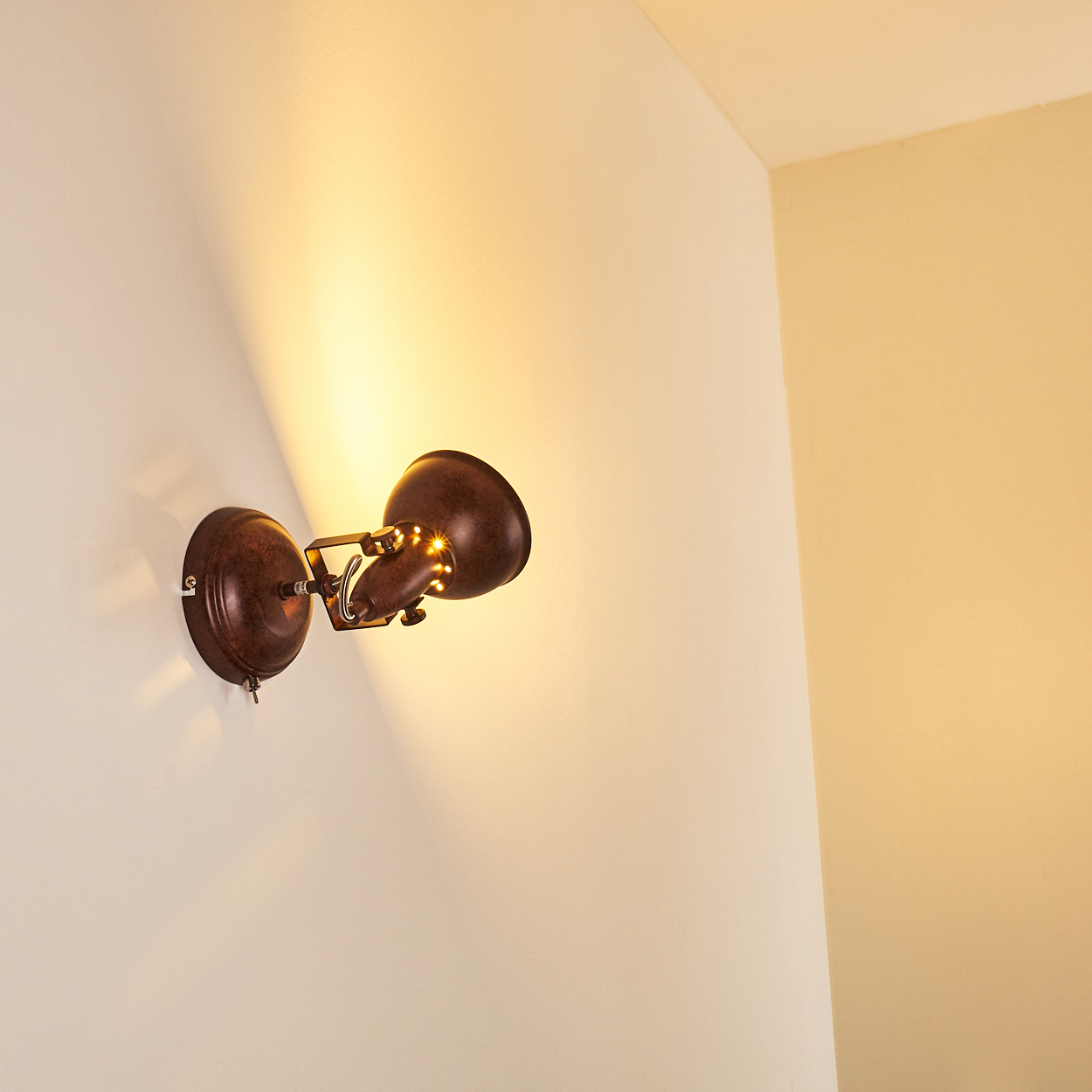 Eine braune Wandleuchte mit mehreren kleinen Lichtern leuchtet auf einer weißen Wand.